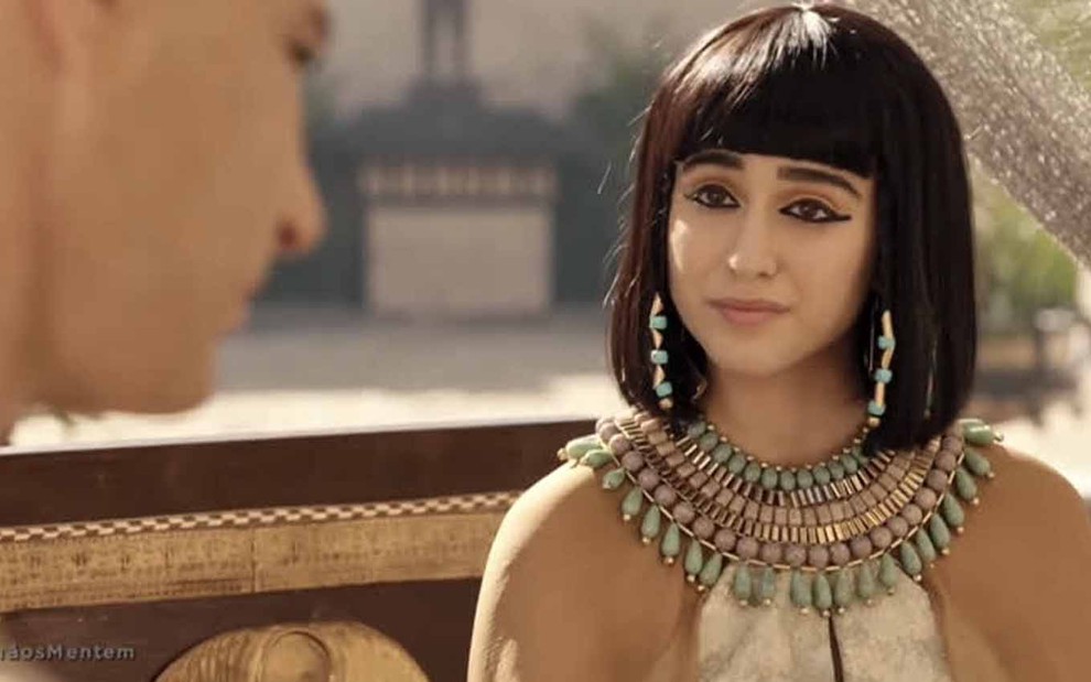 A atriz Marianna Alexandre está com um figurino egípcio ricamente adornado de ouro e pedras verdes com uma peruca de franja, na altura do pescoço, como a Amarilis em Gênesis
