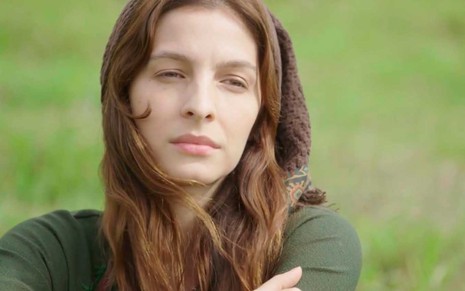 A atriz Michelle Batista como Lia, ela está com expressão triste, em um campo com grama verde em cena de Gênesis