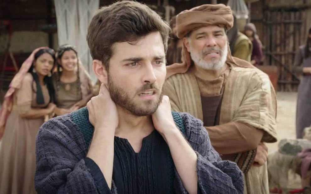 O ator Miguel Coelho leva as mãos ao pescoço, em sinal de tensão, com expressão preocupada, como Jacó de Gênesis