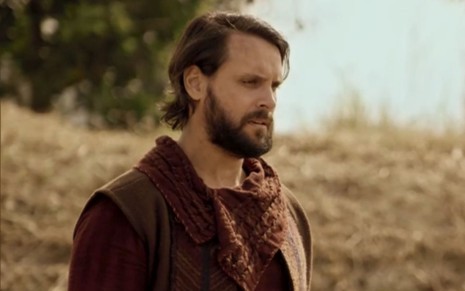 Felipe Cunha caracterizado como Rúben em cena de Gênesis: ator está em pasto com folhas secas