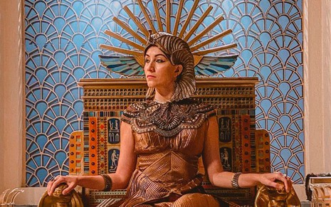 A atriz Samia Abreu está sentada no trono de Sheshi (Fernando Pavão) e olha para a esquerda como Merianat em cena de Gênesis