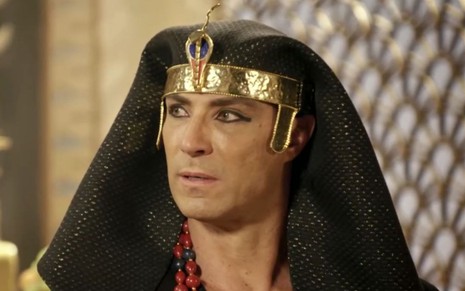 Fernando Pavão em cena de Genesis: ator está caracterizado como Sheshi, usa adorno na cabeça e olha com desconfiança para alguém fora do quadro