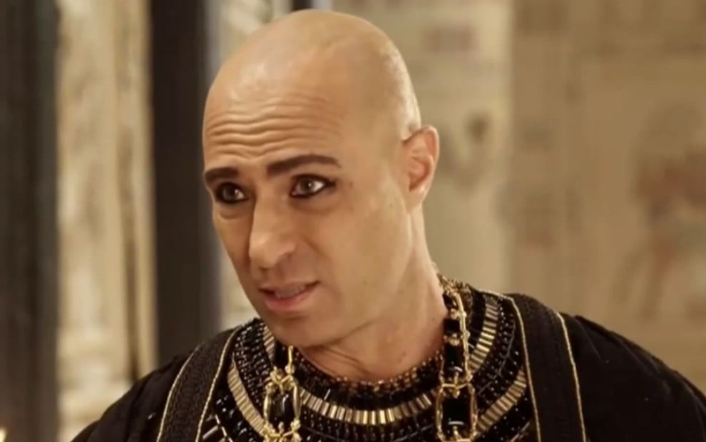 Fernando Pavão caracterizado como Sheshi em cena de Gênesis; ator está com túnica preta e colar dourado no pescoço