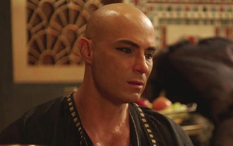 Fernando Pavão caracterizado como Sheshi em cena de Gênesis: ator olha cabisbaixo para alguém fora do quadro