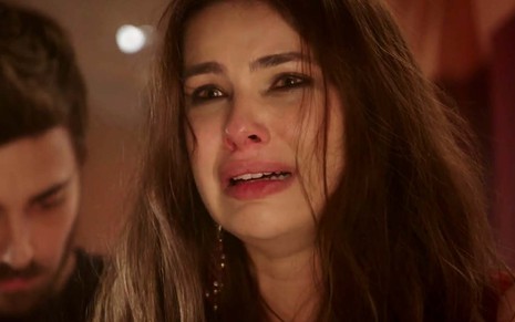 A atriz Thaís Melchior como Raquel em um close-up no seu rosto, com expressão de choro, e descabelada como a Raquel em cena de Gênesis