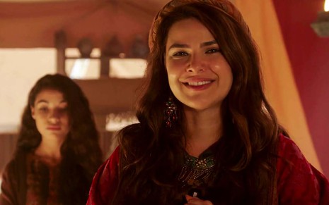 A atriz Thaís Melchior está dentro de uma tenda, com um sorriso cínico, como a Raquel em cena de Gênesis