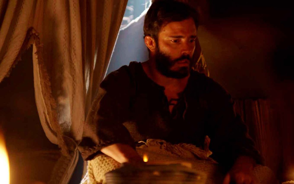 O ator Thiago Rodrigues sentado em uma cama como o Judá com expressão assustada em cena de Gênesis