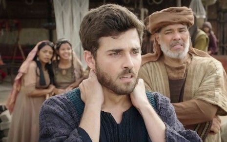 Miguel Coelho em cena de Gênesis: ator está caracterizado como Jacó, coloca as duas mãos na nuca e olha com seriedade para alguém fora do quadro
