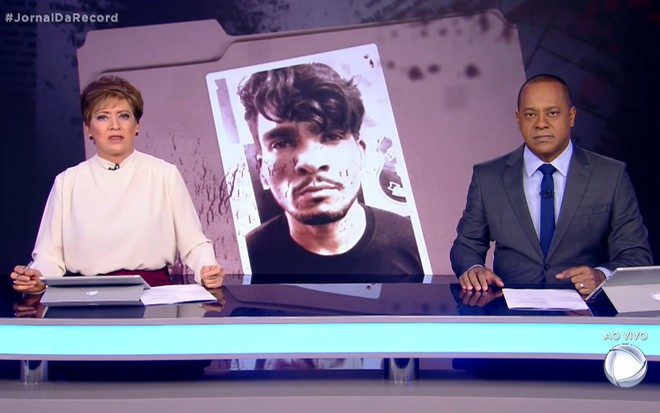 Christina Lemos e Luiz Fara Monteiro estão na bancada do Jornal da Record, com foto de Lázaro Barbosa no telão entre eles