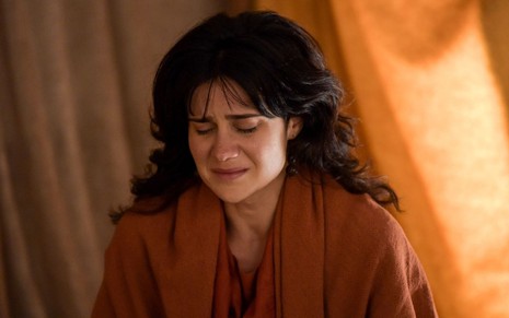 Branca Messina em cena de Reis: caracterizada como Ana, atriz usa bata bege tijolo e faz expressão de choro com os olhos fechados