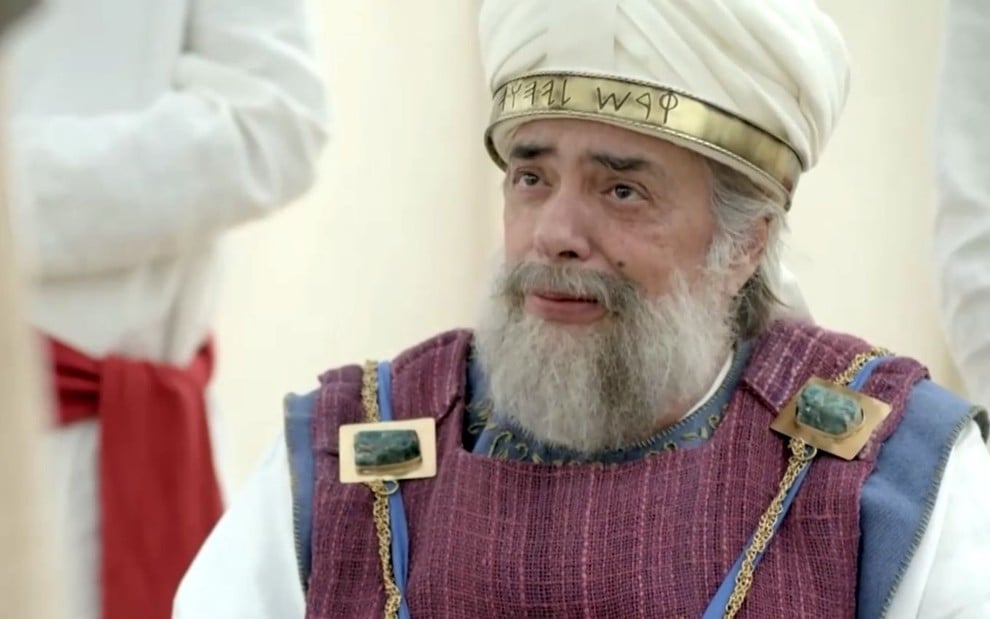 José Rubens Chachá em cena de Reis: ator está sentado, com barba grisalha e usa turbante branco