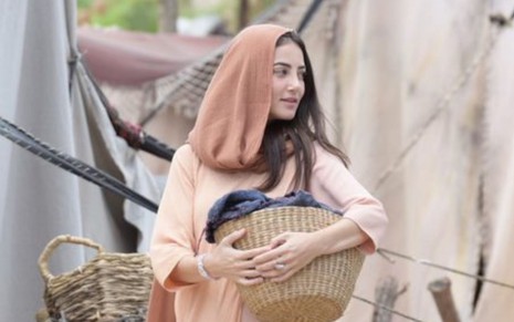 Natália Ferrari grava cena com expressão tensa, segurando cesto, como Sâmila em Reis