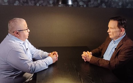 Ricardo Rocha e Roberto Cabrini conversam em mesa dentro de estúdio da Record