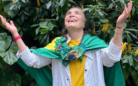 Regina Duarte em foto publicada em seu perfil no Instagram, com bandeira do Brasil amarrada no pescoço, sorrindo abaixo de árvore