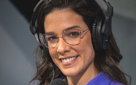 Renata Silveira usa o uniforme azul da Globo nos bastidores de transmissão esportiva; ela está sorridente