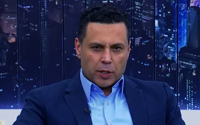 Renato Cardoso com uma blusa azul e terno azul durante o programa Entrelinhas, produzido pela IURD e exibido na Record