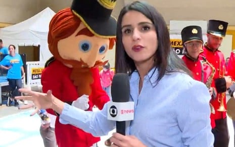 Fernanda Elnour está com um microfone da Globo e gesticula
