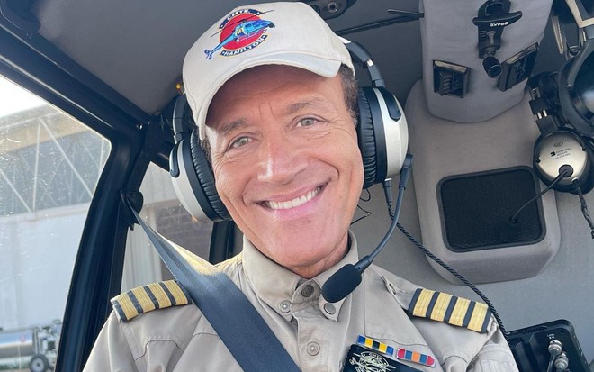 Comandante Hamilton usa uniforme e está dentro de helicóptero; ele sorri na foto