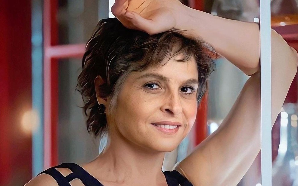A atriz Drica Moraes, com o braço apoiado na cabeça e sorrindo