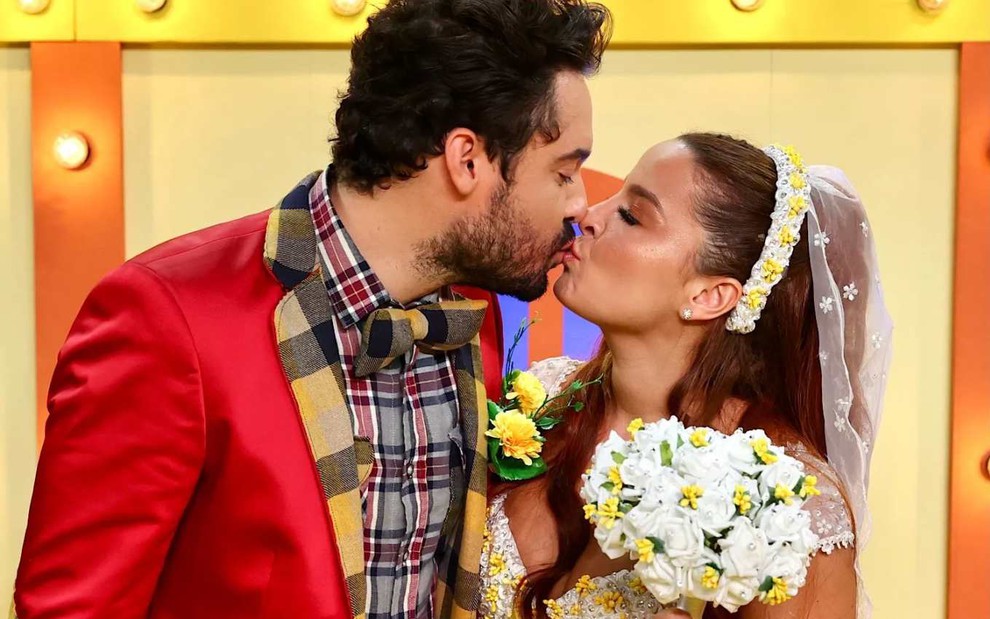 Os cantores Fernando Zor e Maiara, vestidos com roupa de festa junina, dando um beijo