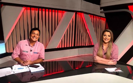 Rhodes Lima, à direita, e Ana Hissa, à esquerda, no estúdio do canal Combate usando uma camisa rosa e sorrindo para a foto