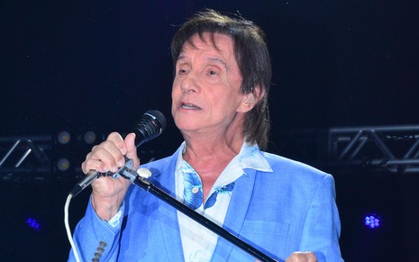 O cantor Roberto Carlos segura um microfone de forma característica durante show com paletó azul e camisa branca