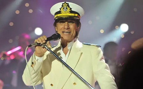 Roberto Carlos no palco do projeto Emoções: cantor está vestido de capitão e canta com um microfone em um pedestal