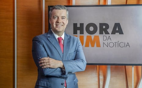 Roberto Kovalick com um terno azul, uma camisa branca e uma gravata vermelha nos estúdios do Hora 1, da Globo