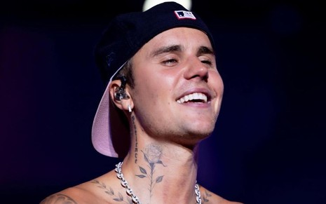 O cantor Justin Bieber, sorri de boné e sem camisa durante apresentação musical