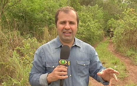 Repórter Rodrigo Hidalgo, da Band, fala para a câmera segurando um microfone em um matagal