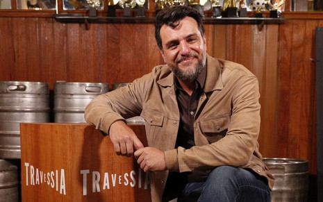 Rodrigo Lombardi sentado em uma cadeira no cenário de um bar em Travessia