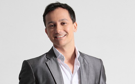 O apresentador Rodrigo Ruas com um terno cinza e camisa branca sorrindo para a câmera