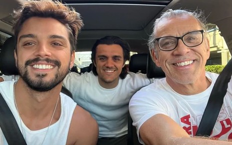 Rodrigo Simas está no banco de passageiro; Felipe, no banco traseiro; e Beto no assento de motorista. Eles sorriem para a câmera.