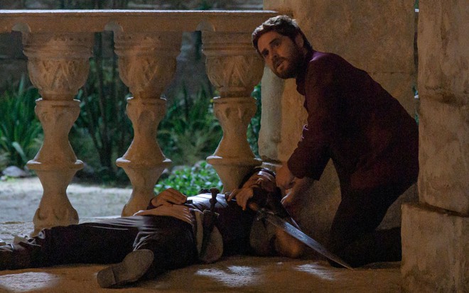 Roger Gobeth está deitado no chaõ, e Cirillo Luna meche com ele em cena da novela Reis