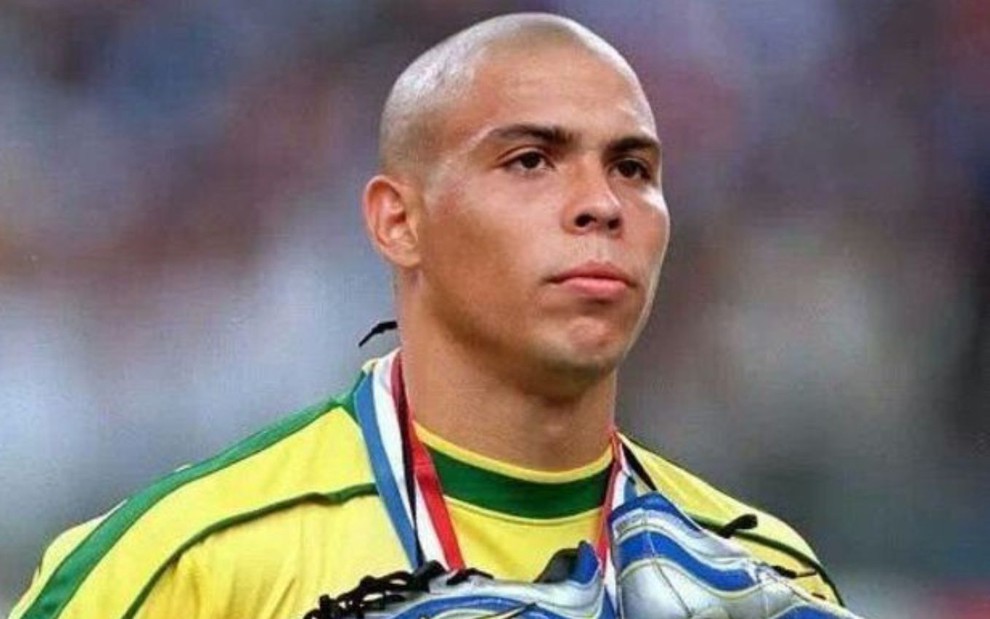 Ronaldo Fenômeno em jogo do Brasil com as chuteiras amarradas no pescoço e camisa amarela com detalhes verdes