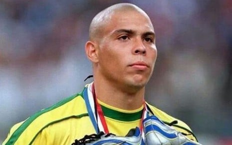 Ronaldo Fenômeno em jogo do Brasil com as chuteiras amarradas no pescoço e camisa amarela com detalhes verdes