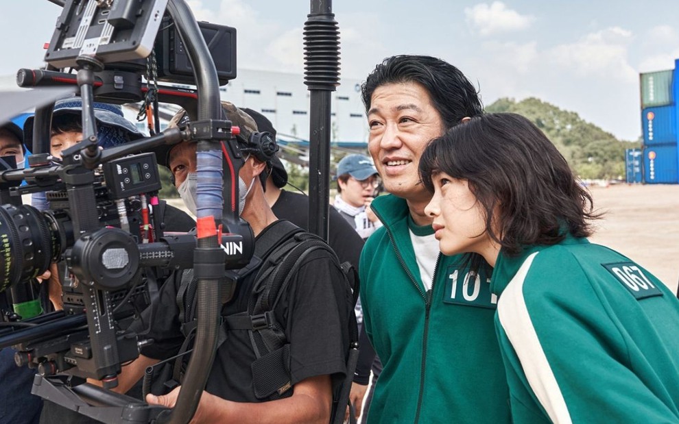 Os atores Heo Sung-tae e Hoyeon Jung sorriem para a câmera nos bastidores de Round 6, série da Netflix