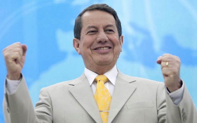 R.R Soares com uma gravata amarela, terno cinza e celebrando um culto no programa Show da Fé
