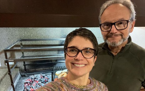 Sandra Annenberg e Ernesto Paglia sorrindo em frente a churrasqueira