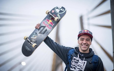 Sandro Dias, o Mineirinho, sorri para a câmera e mostra um skate com a marca da empresa Red Bull, que lhe patrocina