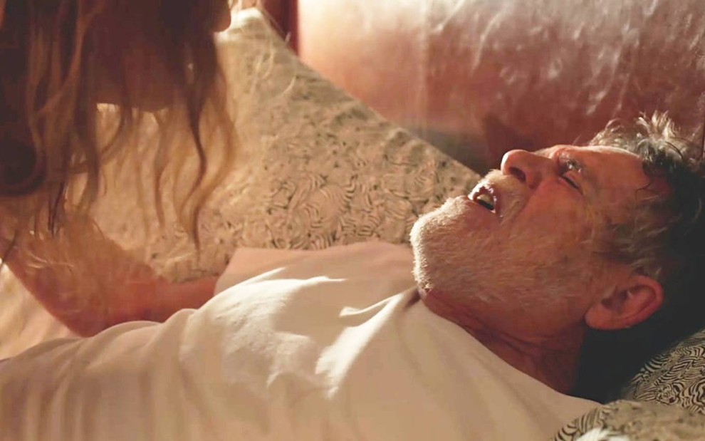 Ator José de Abreu surge deitado na cama e faz cara de dor em cena de Um Lugar ao Sol