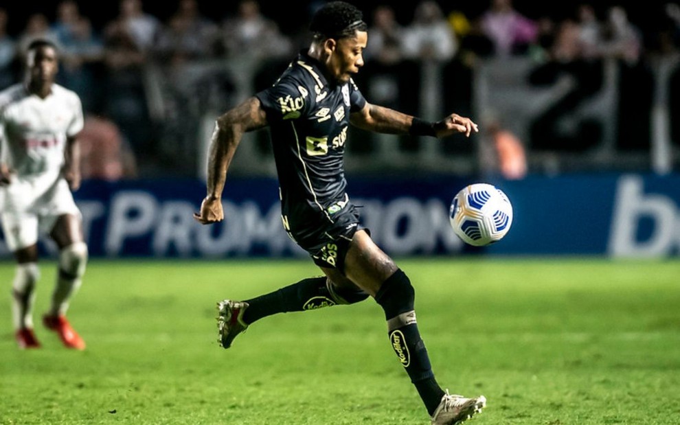 Jogador Marinho, do Santos, vestindo uniforme preto com dourado e dominando a bola durante partida