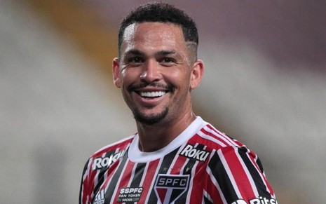 Luciano, do São Paulo, com bola debaixo do braço, veste uniforme listrado em vermelho, preto e branco
