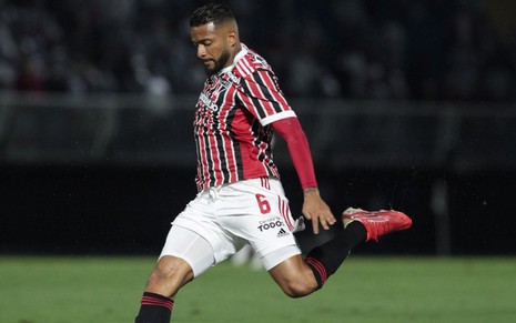 Jogador Reinado, do São Paulo, vestindo uniforme listrado em preto, vermelho branco, chutando a bola