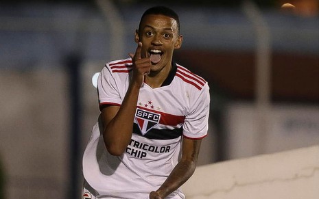 Jogador Caio, do São Paulo, veste uniforme branco com detalhes vermelho e preto e comemora gol feito