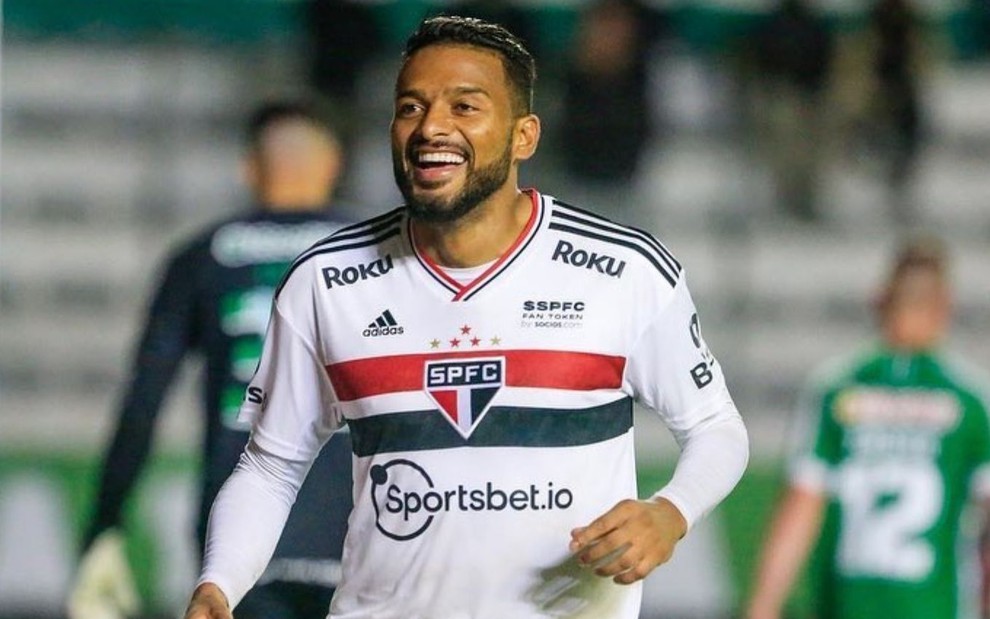 Reinaldo, do São Paulo, sorri ao comemorar gol e veste uniforme branco com faixas vermelha e preta