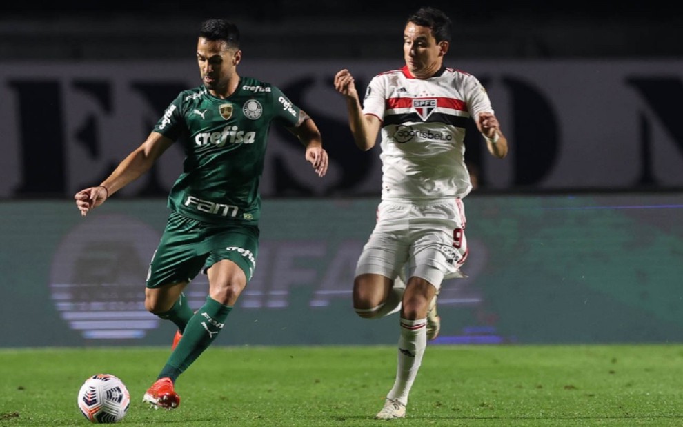 Raphael Veiga e Pablo, jogadores de Palmeiras e São Paulo, brigam pela bola. Raphael usa uma camisa verde, enquanto Pablo usa o branco com listras vermelhas e pretas