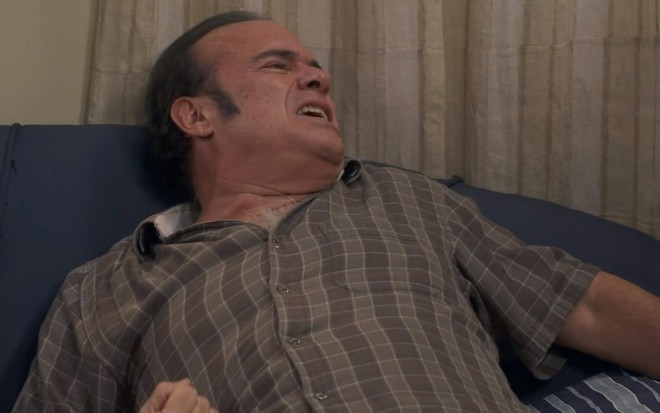 André Mattos faz careta de dor enquanto se joga em um sofá em cena de A Infância de Romeu e Julieta