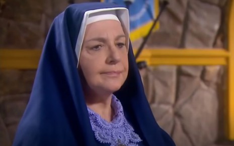 Eliana Guttman grava cena vestida de freira, com expressão séria, como Madre Superiora em Carinha de Anjo, do SBT