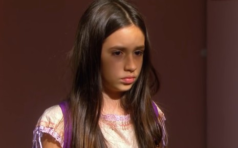 Bianca Paiva grava com cabelo solto, mochila nas costas e expressão de tristeza como Lucia de Chiquititas, do SBT